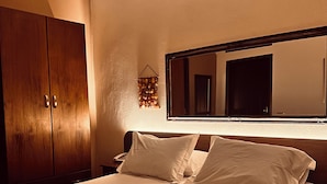 Ein ordentlich bezogenes Bett mit Kissen, ein Holzschrank und ein wandmontierter Spiegel.