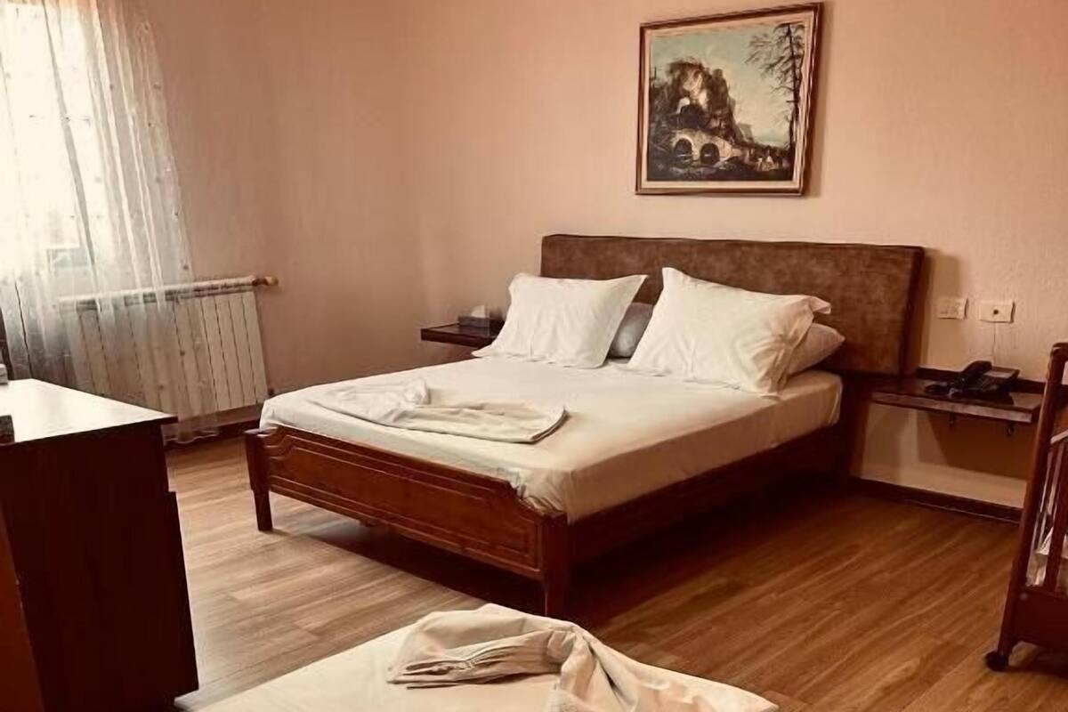 A hotel room with a bed, bedside table, and a painting on the wall.