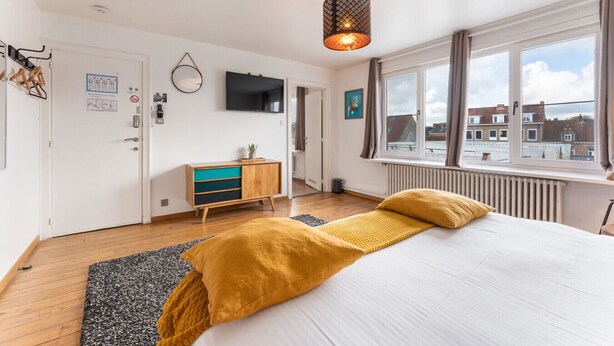 A bedroom with a bed, a TV, a window, and a radiator.