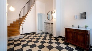 A staircase with wooden steps and a metal railing, a checkered floor, a white wall with a mirror, and a wooden cabinet with a marble countertop.
