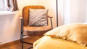 A chair with a cushion, a window with curtains, and a bed with a pillow.