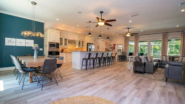 A spacious living area with a dining table, chairs, sofas, and a kitchen in the background.