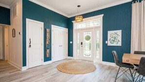 A hallway with a round woven rug, white doors, a dining area with a table and chairs, and a wall-mounted light fixture.