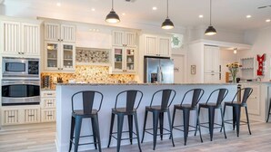 A kitchen with white cabinetry, a central island with bar stools, a microwave, and a refrigerator.