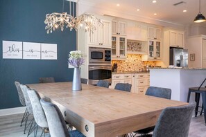 Une cuisine moderne avec des meubles blancs, des appareils en acier inoxydable et une table à manger en bois, accompagnée de chaises.