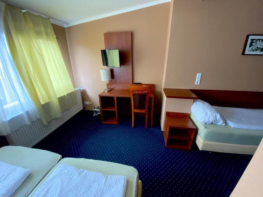 Ein Hotelzimmer mit zwei Betten, einem Schreibtisch mit Stuhl, einem Fernseher und einem kleinen Tisch.