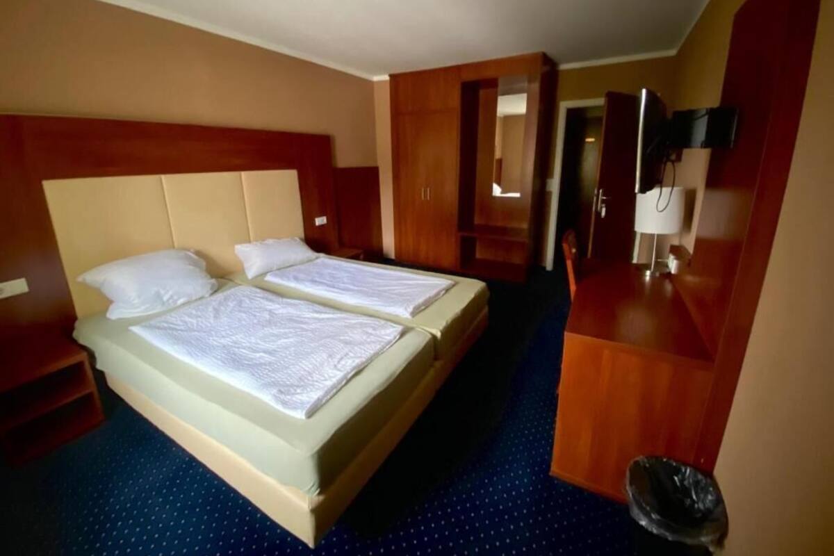 A hotel room with two beds, a wooden headboard, a desk with a chair, a mirror, and a trash bin.