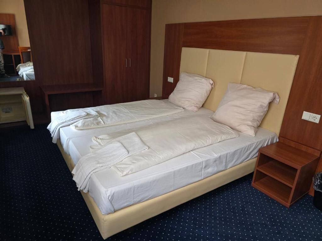 A double bed with a wooden headboard, a bedside table, and a wardrobe in a hotel room.