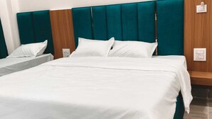 A hotel room with a large bed, a smaller bed, wooden paneling, teal headboard, and a wooden door. - Majestic Ganges (Haridwar)