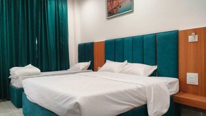 A hotel room with two beds, teal curtains, a wooden headboard, and a painting on the wall. - Majestic Ganges (Haridwar)