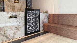 A reception area with a marble wall, a black and white patterned partition, a brown sofa, and a clock on the wall. - Majestic Ganges (Haridwar)
