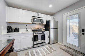 Una cocina moderna con armarios blancos, un refrigerador de acero inoxidable, un microondas, una estufa y una cafetera.