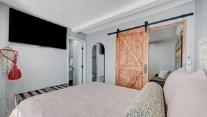 A bedroom with a large bed, a TV mounted on the wall, a sliding barn-style door, and a mirror reflecting the room. - 1BR Casita, Central Location + Private Bkyd + Free Uber Airport Pickup (Las Vegas)
