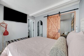 Un dormitorio con una cama grande, un televisor montado en la pared, una puerta corredera de estilo granero y un espejo que refleja la habitación.