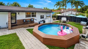 Ein Garten mit Whirlpool, einer überdachten Terrasse und einem Pool mit aufblasbaren Einhorn-Schwimmfiguren.