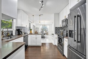 A modern kitchen with white cabinets, stainless steel appliances, and a central island. - VIP Concierge • Pool, BBQ, Bikes • Airport 5 mins (Fort Lauderdale)