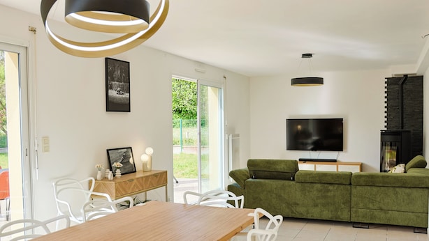 Uma sala de estar moderna com uma mesa de jantar de madeira, cadeiras brancas, um sofá verde, uma televisão de tela plana e uma lareira.