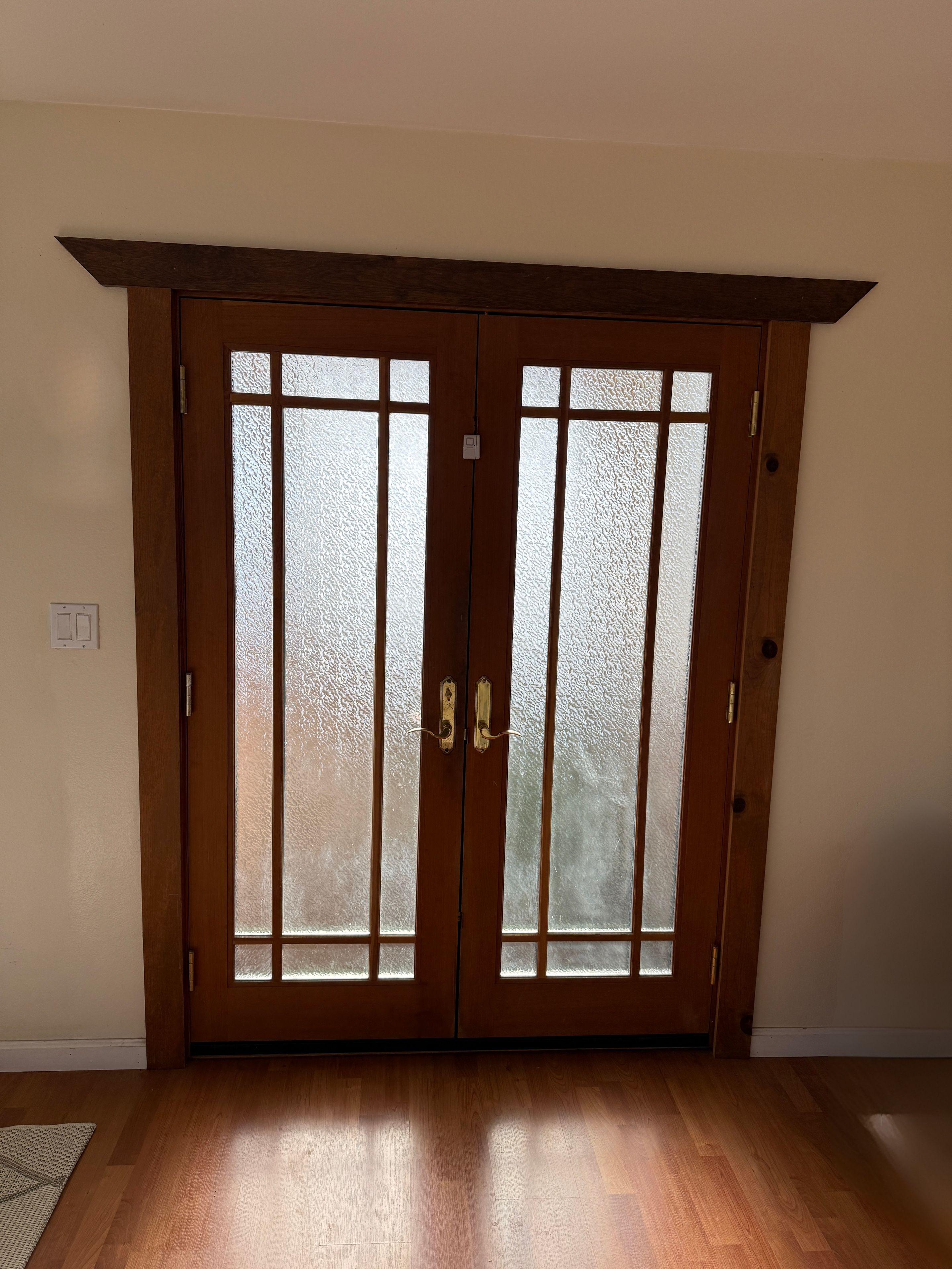 Puerta doble de madera con paneles de vidrio satinado y un tirador.