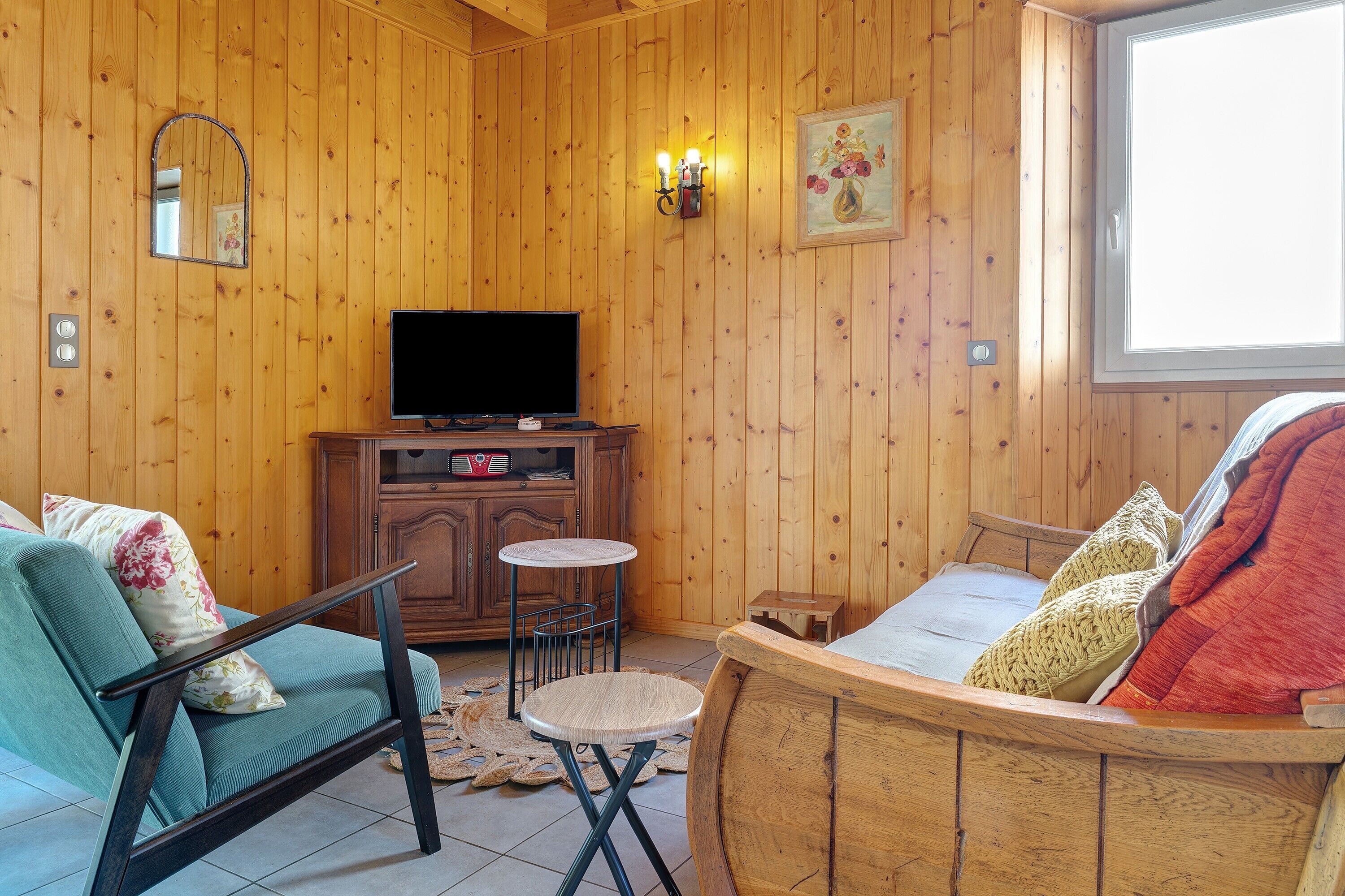 A wooden-paneled room with a television, a sofa, a small round table, and a bed with pillows.