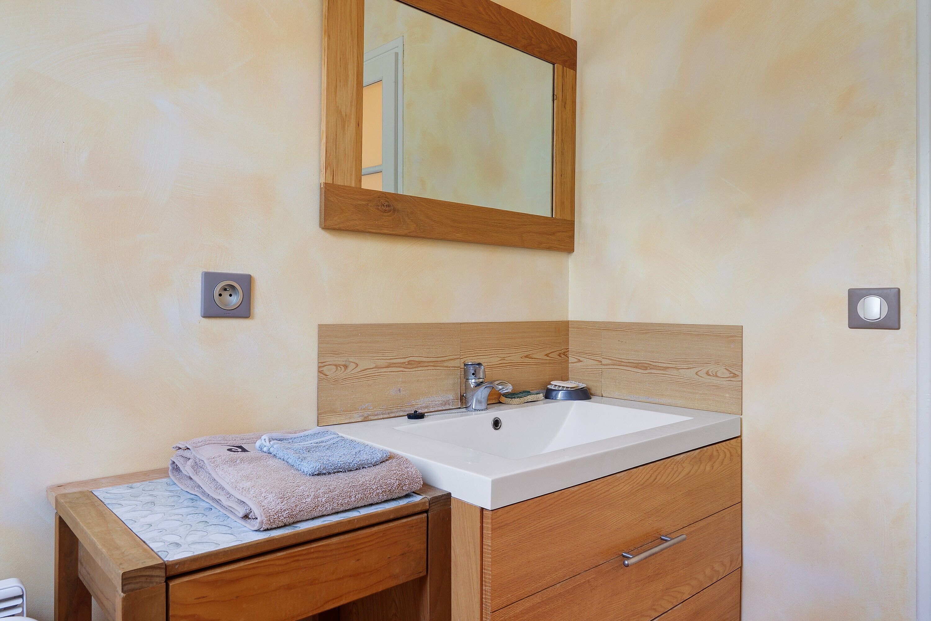 A bathroom with a wooden vanity, a sink, a mirror, and a towel.