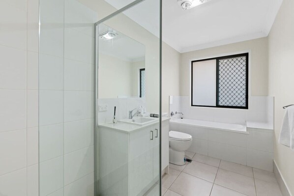 A modern bathroom with a glass shower enclosure, a white sink, a toilet, and a bathtub. - Spacious Family Retreat| Near Hospital & Hyperdome (Loganlea)