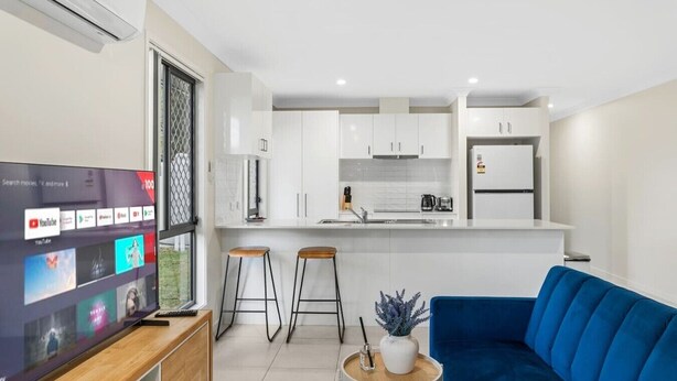 Une cuisine moderne avec des meubles blancs, un îlot central et un canapé bleu.