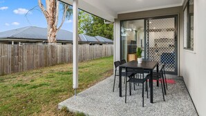 Une terrasse couverte avec une table et des chaises, une clôture en bois et un arbre.