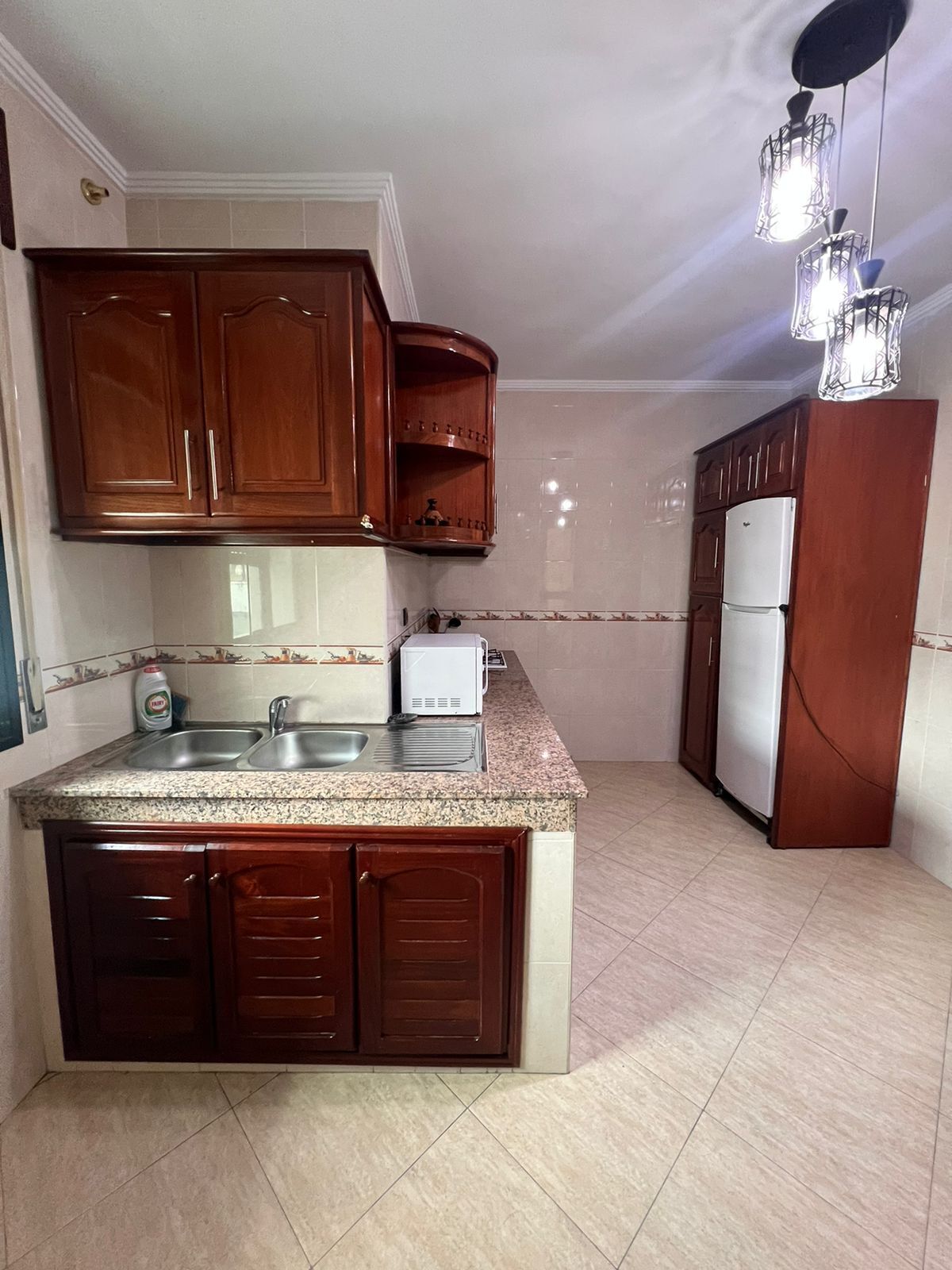 A kitchen with wooden cabinets, a granite countertop, a sink, a toaster, and a refrigerator.