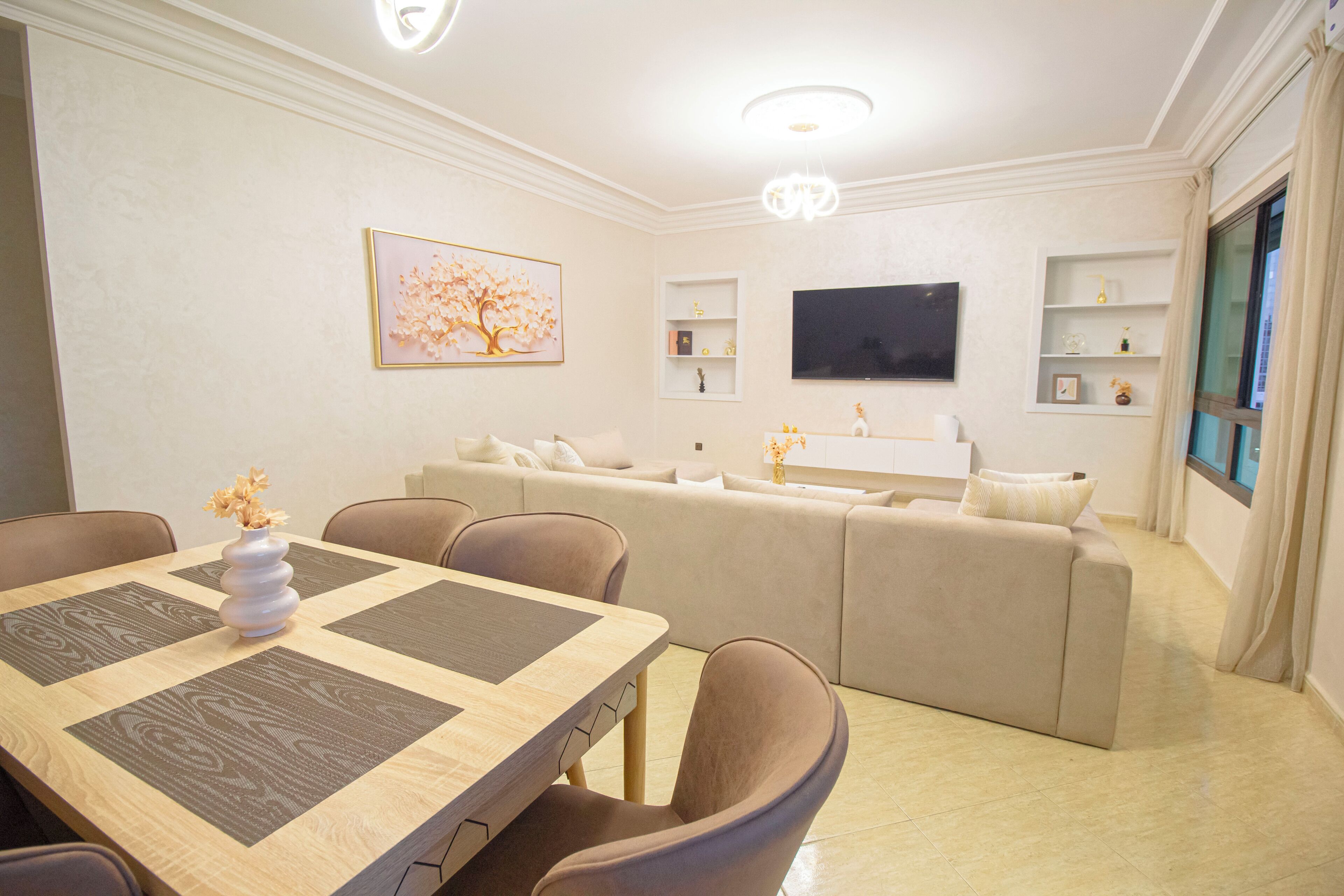 A modern living room with a dining area, a sofa set, a flat-screen TV, and decorative shelves.