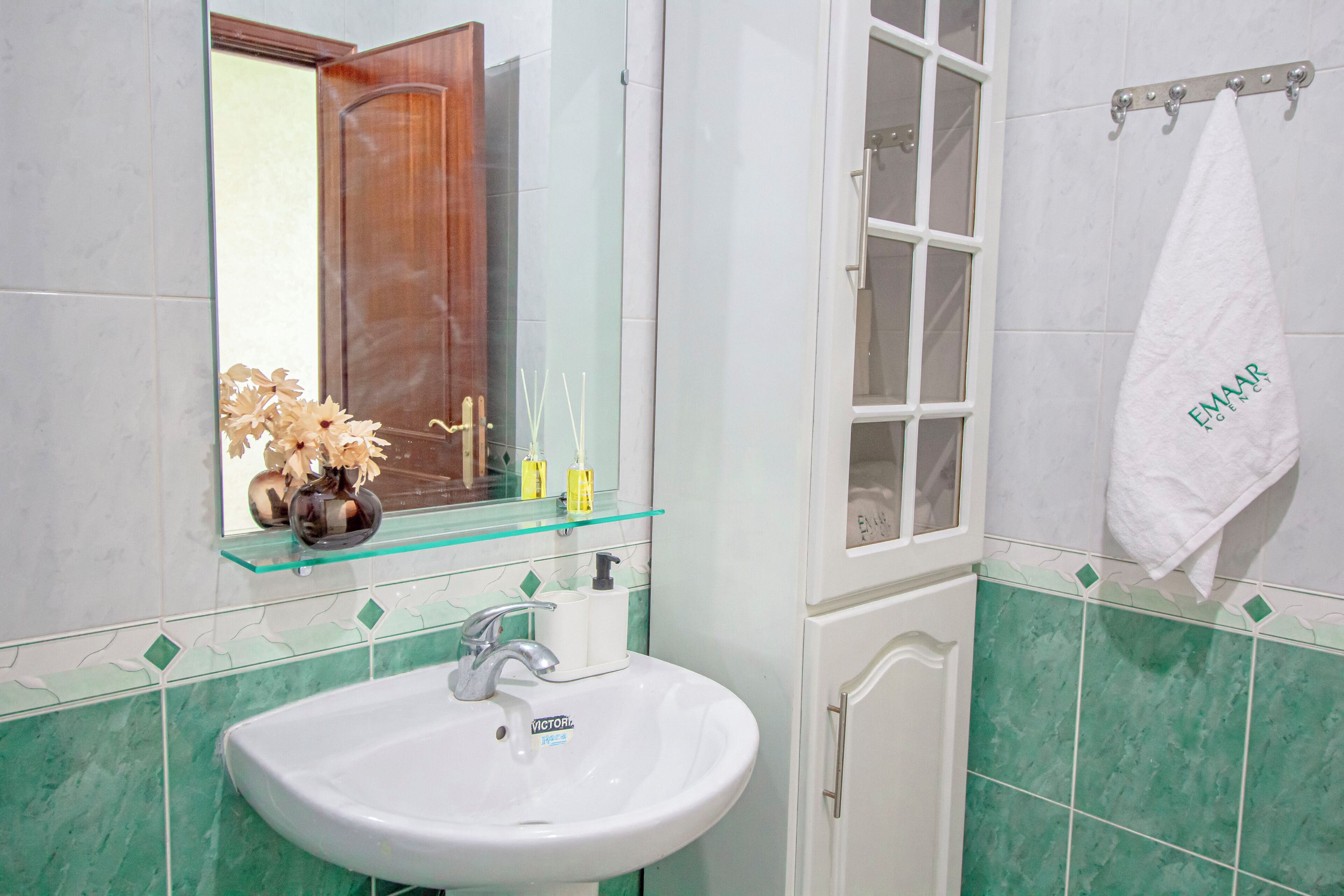 A bathroom with a white sink, a glass shelf with toiletries, a mirror, and a towel rack.