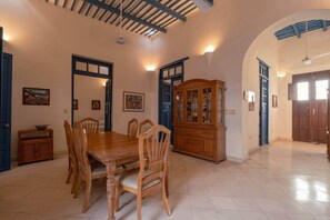 A dining area with a wooden table and chairs, a cabinet, and a ceiling with exposed beams. - Casa Luz: Cozy Retreat + Pool (Mérida)