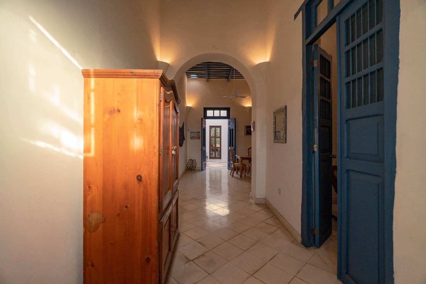 A hallway with a wooden cabinet, a blue door, and an arched ceiling.