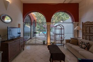 A living room with a TV, sofa, and a gate leading to an outdoor area with a pool. - Casa Luz: Cozy Retreat + Pool (Mérida)
