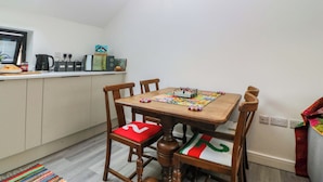 A dining area with a wooden table, chairs, and a hanging light fixture. - Trwyn Cam (Caernarfon)