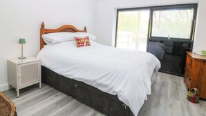 A bedroom with a bed, a nightstand, a lamp, a window, and a view of the outside. - Trwyn Cam (Caernarfon)