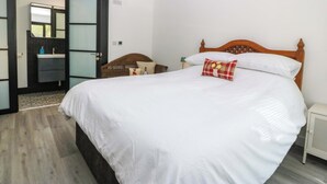 Un dormitorio con una cama grande, cabecera de madera, mesita de noche, lámpara de noche, un espejo y un baño con lavamanos e inodoro.
