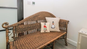 A wicker sofa with a cushion featuring a cartoon character, a thermostat, and a cabinet with a heart design. - Trwyn Cam (Caernarfon)
