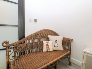 Un sofá de mimbre con un cojín que muestra un personaje de caricatura, un termostato y un mueble con diseño de corazón.