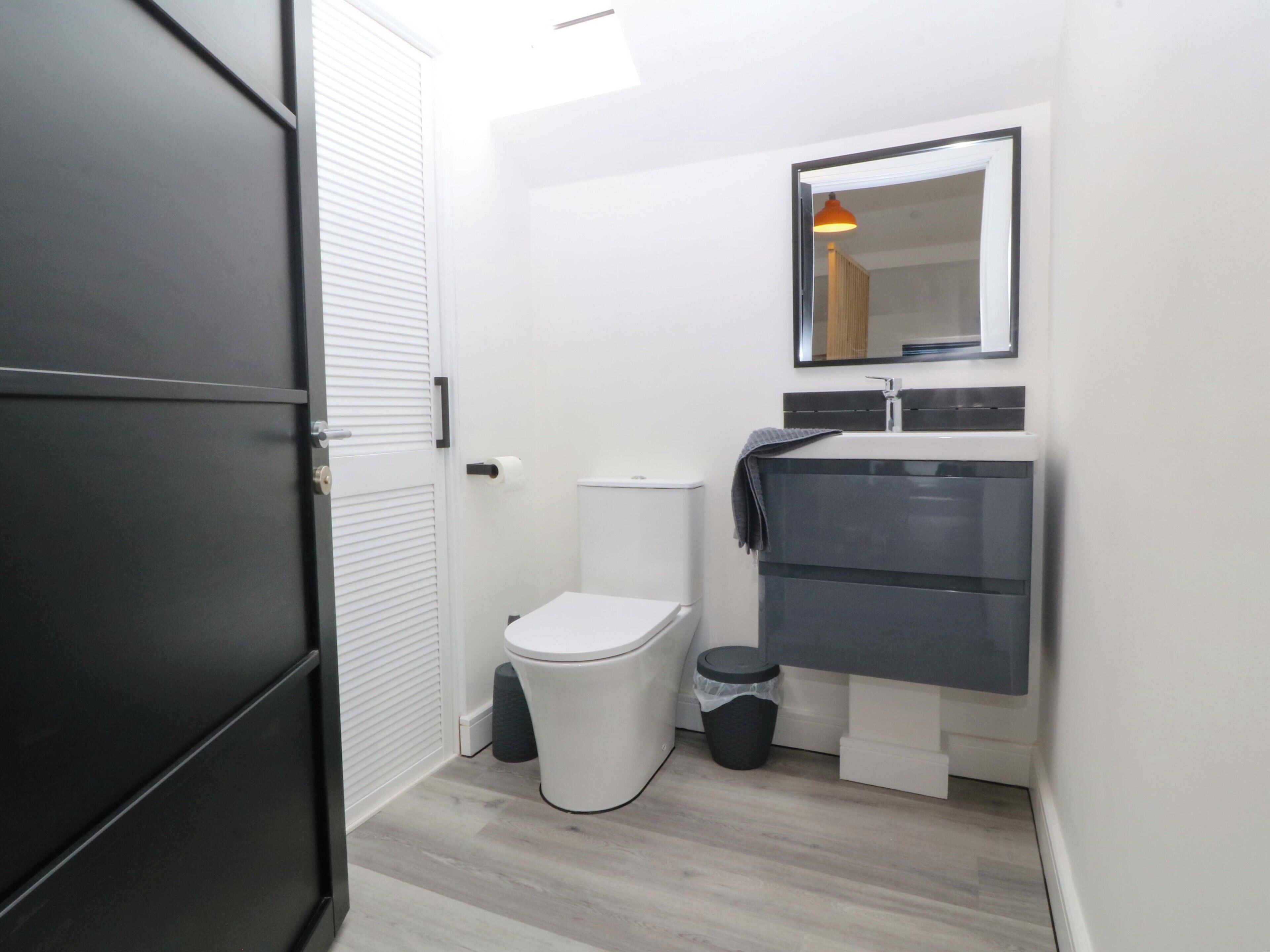 A modern bathroom with a toilet, sink, mirror, and a trash bin.