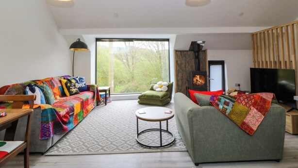 A modern living room with a sofa, a green armchair, a round coffee table, and a fireplace. - Trwyn Cam (Caernarfon)