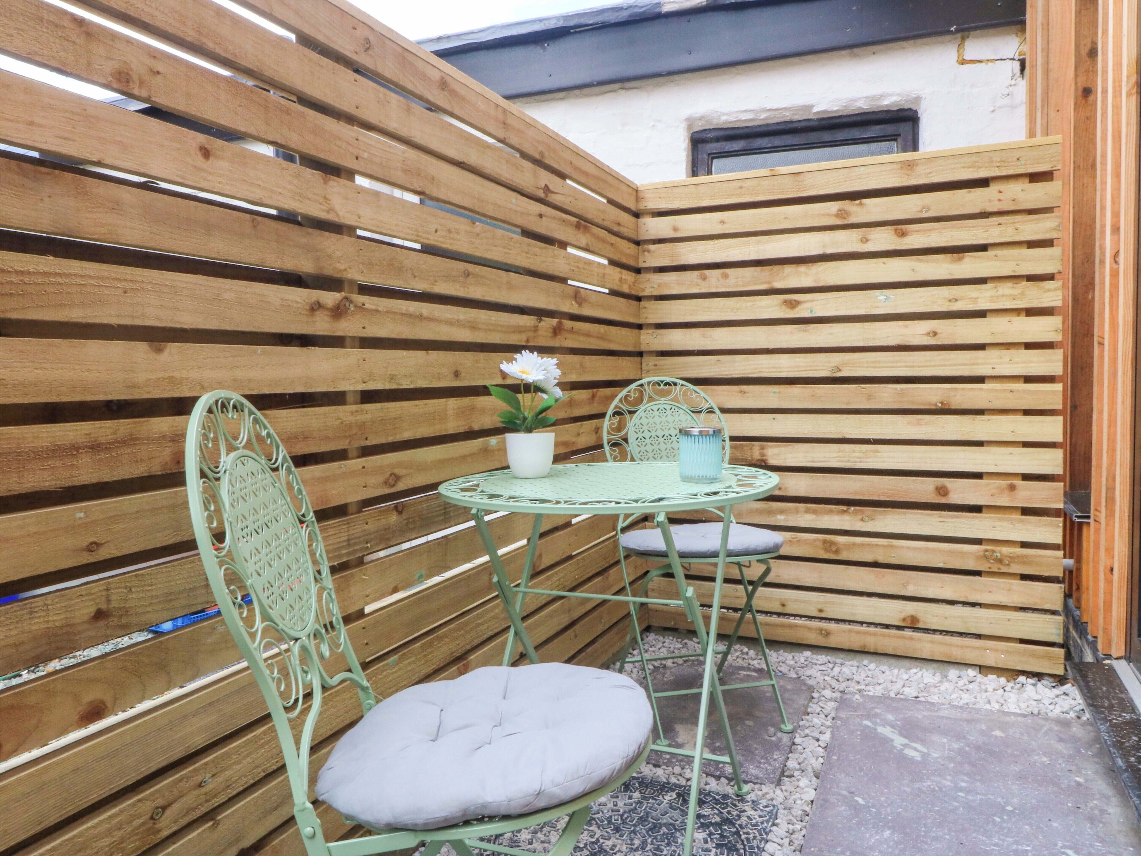 Un pequeño espacio al aire libre con una mesa y sillas de metal, una planta en maceta y una valla de madera.