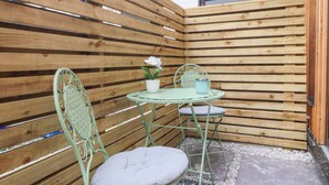 Un pequeño espacio al aire libre con una mesa y sillas de metal, una planta en maceta y una valla de madera.