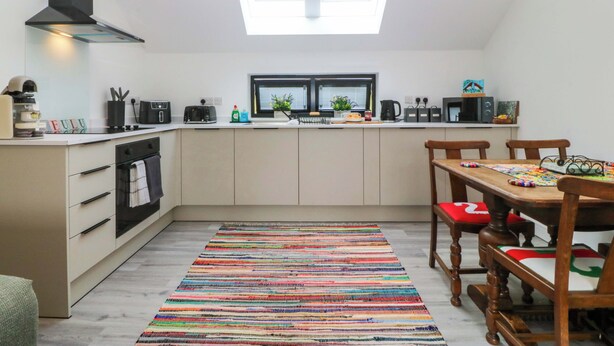 Una cocina moderna con tragaluces, un área de comedor con un tapete colorido y sillas de madera.