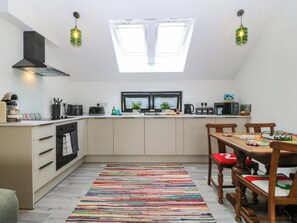 A modern kitchen with a skylight, a dining area with a colorful rug, and wooden chairs. - Trwyn Cam (Caernarfon)