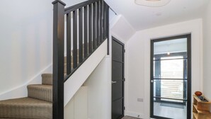A staircase with a black handrail, a white door with a glass panel, and a wooden shelf with a football. - Trwyn Cam (Caernarfon)