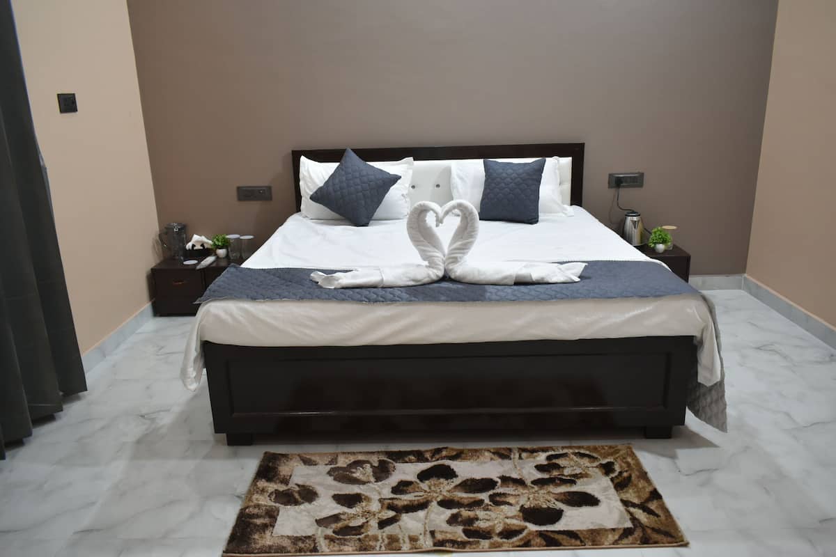 A neatly made bed with a heart-shaped towel arrangement, a dark wooden headboard, a marble floor, and a patterned rug.