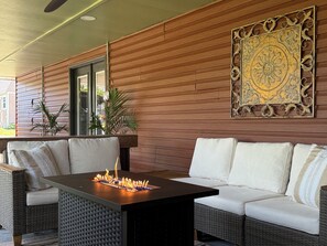 A covered outdoor seating area with a fire feature, wicker furniture, and a decorative wall panel. - SoHo-Lakeside Retreat (Abingdon)