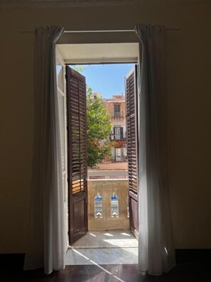 An open doorway with wooden shutters, leading to an outdoor area with buildings and a tree. - Nowhere Rooms (Palermo)