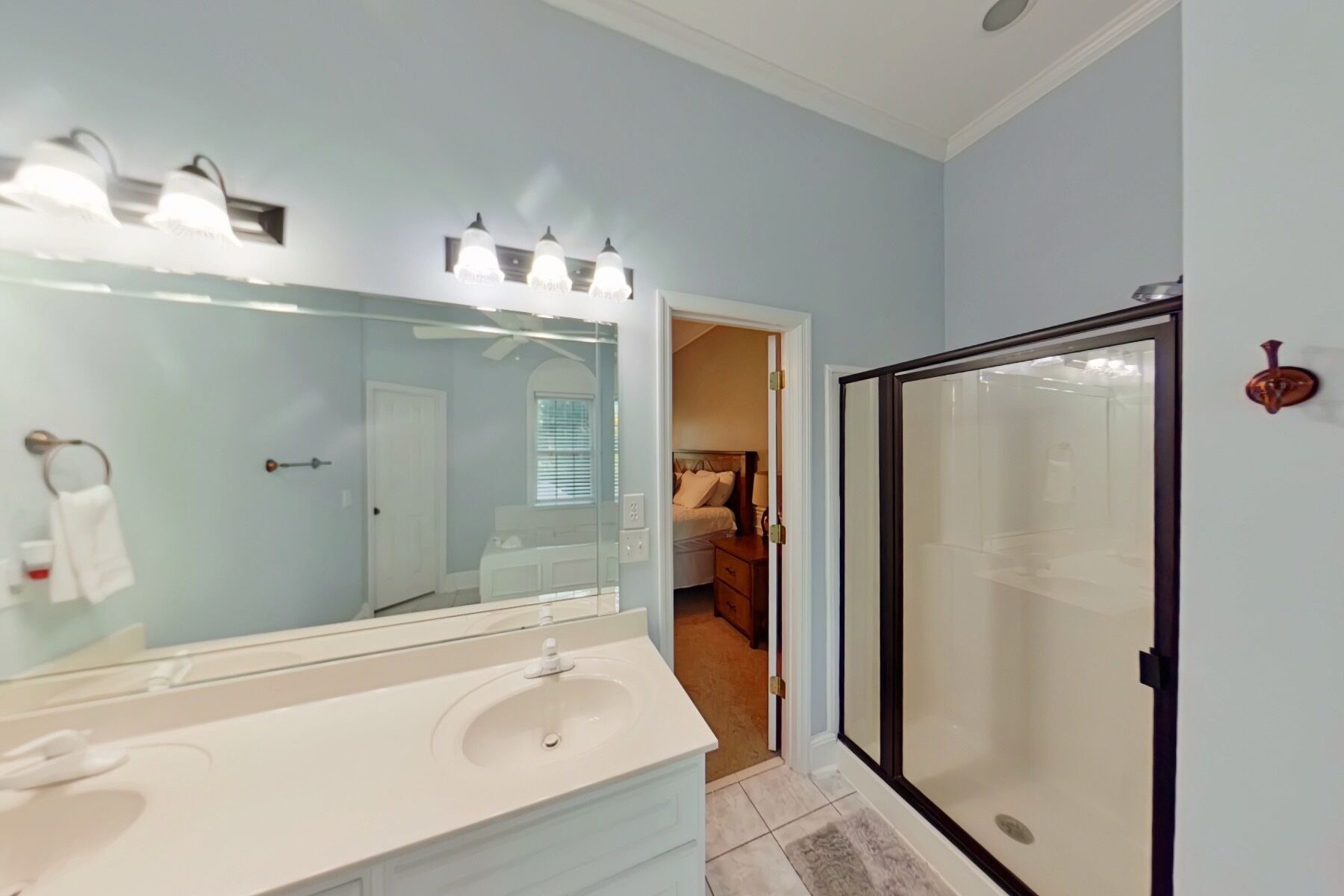 A bathroom with a large mirror, a white sink, and a shower with a glass door.