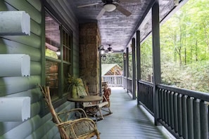 Une véranda avec une table et des chaises, une lanterne, et une vue sur une maison en arrière-plan.